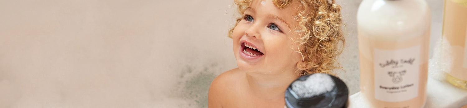 Child in a bathtub with a bottle of baby soap and shampoo.