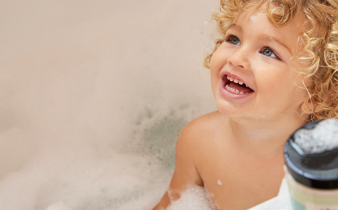 Child in a bathtub with bubbles, holding a toy.